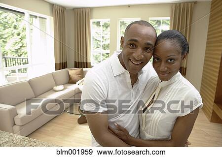 Stock Photo - African couple hugging and smiling in livingroom. Fotosearch
