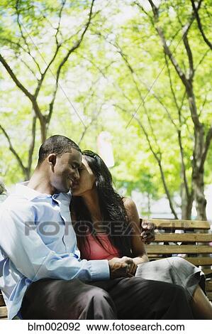 Stock Image - African couple hugging on bench. Fotosearch