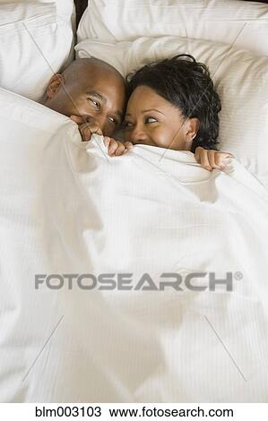 Stock Image - African couple in bed under blanket. Fotosearch
