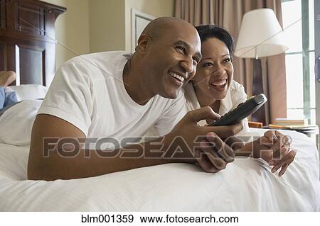 Stock Photo - African couple in bed watching television. Fotosearch