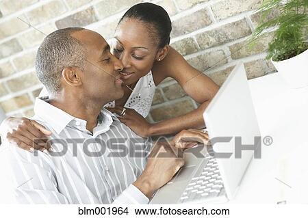 Picture - African couple kissing next to laptop. Fotosearch