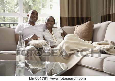 Stock Image - African couple on sofa eating popcorn. Fotosearch