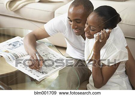 Stock Photo - African couple reading classifieds and talking on telephone. Fotosearch
