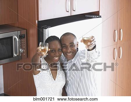 Stock Image - African couple toasting with wine in kitchen. Fotosearch