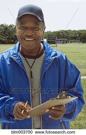 Stock Image - African football coach holding clipboard on field. Fotosearch