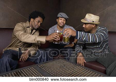Stock Image - African friends toasting with beer in nightclub. Fotosearch