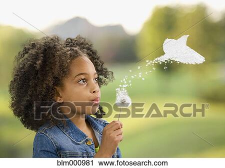 Stock Image - African girl blowing dandelion, seeds turning into bird. Fotosearch