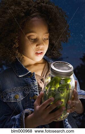Stock Photo - African girl looking at fireflies in jar. Fotosearch