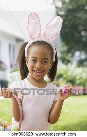 Stock Photo - African girl wearing bunny ears and holding Easter egg. Fotosearch
