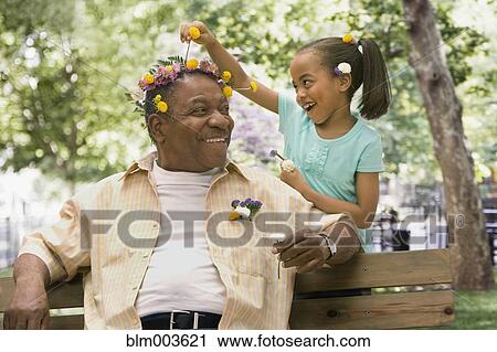 Stock Image - African granddaughter decorating grandfather's head with flowers. Fotosearch