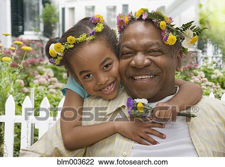 Stock Image - African grandfather and granddaughter hugging with flowers on head. Fotosearch