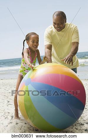 Stock Image - African grandfather and granddaughter playing on beach with large ball. Fotosearch