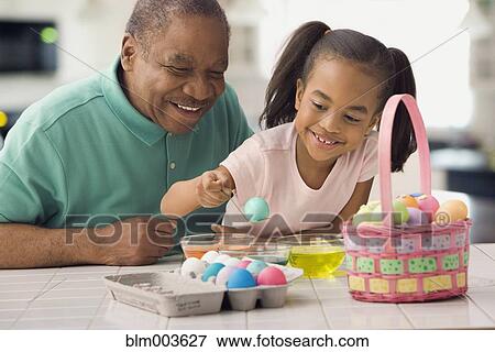 Stock Photo - African grandfather and granddaughter coloring Easter eggs. Fotosearch