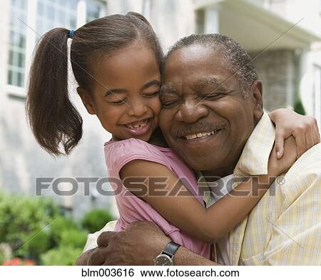 Stock Photograph - African grandfather and granddaughter hugging with eyes closed. Fotosearch
