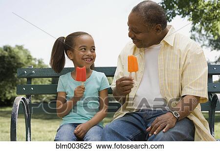 Stock Photography - African grandfather and granddaughter eating ice pops. Fotosearch