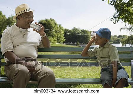 Picture - African grandfather and grandson playing with tin can phone. Fotosearch