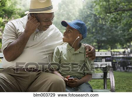 Stock Photo - African grandfather and grandson sharing headphones on park bench. Fotosearch