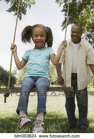 Picture - African grandfather pushing granddaughter on swing. Fotosearch