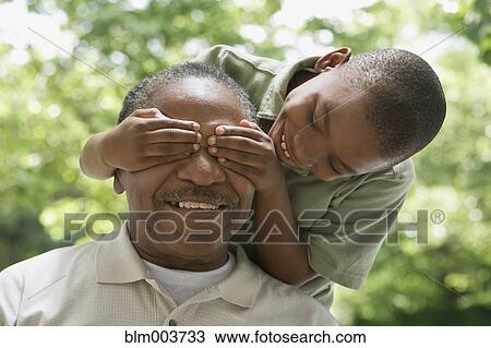 Stock Image - African grandson covering grandfather's eyes. Fotosearch