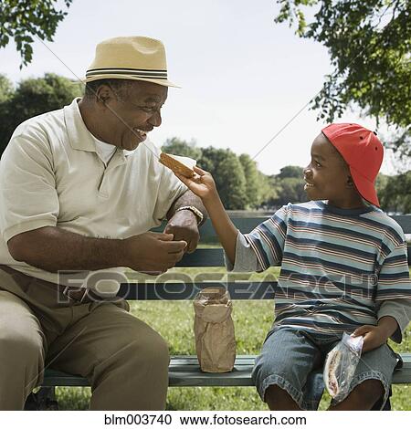 Stock Image - African grandson sharing sandwich with grandfather. Fotosearch