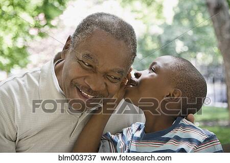 Stock Photo - African grandson whispering in grandfather's ear. Fotosearch