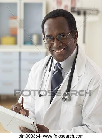 Picture - African male doctor writing on medical chart. Fotosearch