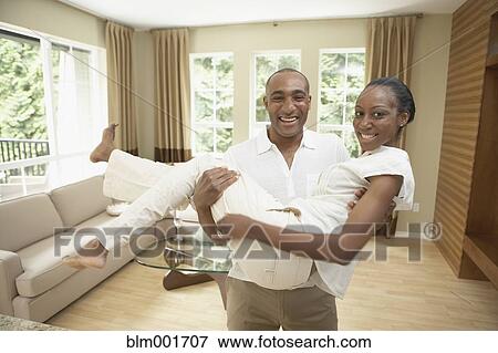 Stock Photo - African man carrying wife in livingroom. Fotosearch