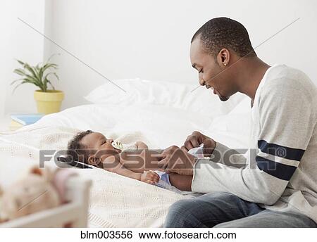 Stock Photograph - African man changing baby's diaper on bed. Fotosearch