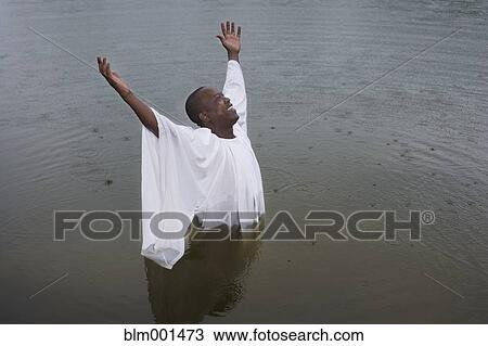 Stock Image - African man getting baptized in lake. Fotosearch