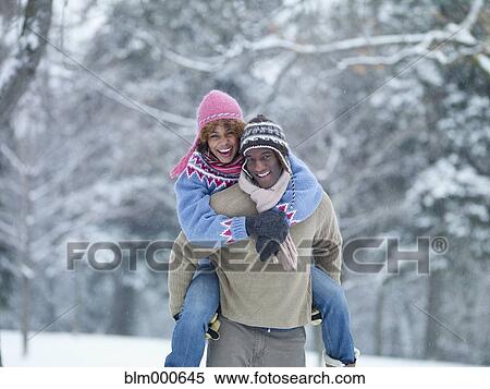 Stock Photography - African man giving girlfriend piggyback ride in snow. Fotosearch