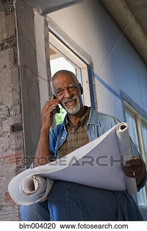 African man holding blueprints and talking on cell phone View Large Photo Image Stock Image - African man holding blueprints and talking on cell phone. Fotosearch