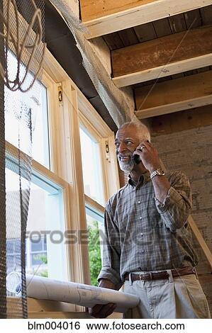 Stock Photograph - African man holding blueprints and talking on cell phone. Fotosearch