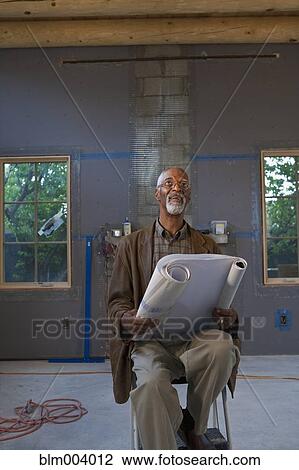 Stock Image - African man holding blueprints at construction site. Fotosearch