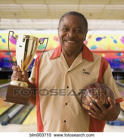 Stock Image - African man holding bowling ball and trophy. Fotosearch