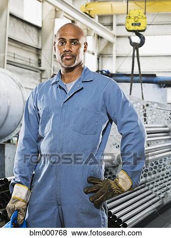 Stock Photo - African man in gloves and coveralls in factory. Fotosearch