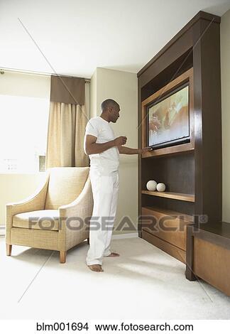 Picture - African man in pajamas turning on television. Fotosearch