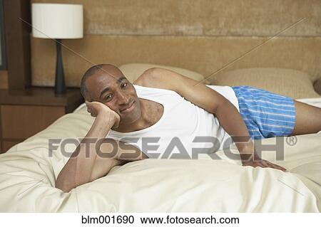Stock Image - African man laying on bed in underwear. Fotosearch
