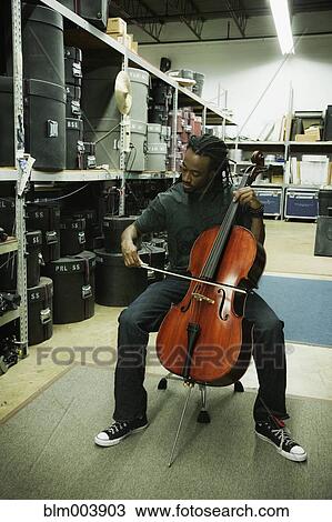 Stock Image - African man playing cello in warehouse. Fotosearch