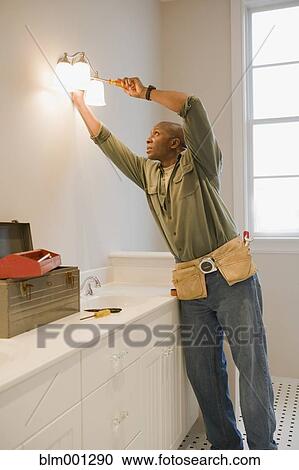 Stock Image - African man repairing light fixture. Fotosearch