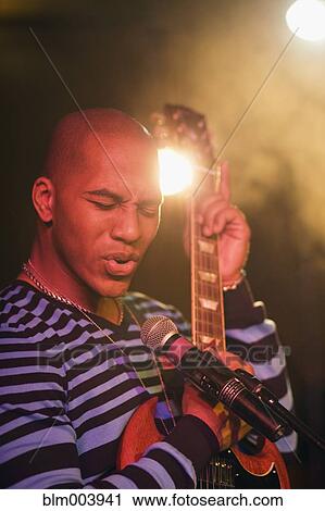 Stock Image - African man singing and playing electric guitar onstage. Fotosearch