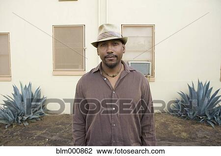 Stock Image - African man standing in front of house. Fotosearch