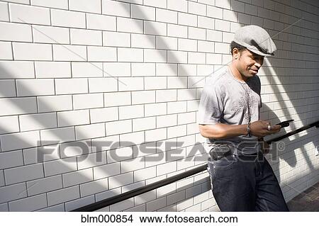 Picture - African man text messaging in urban setting. Fotosearch
