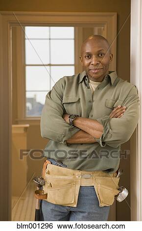 Stock Photograph - African man wearing tool belt with arms crossed. Fotosearch