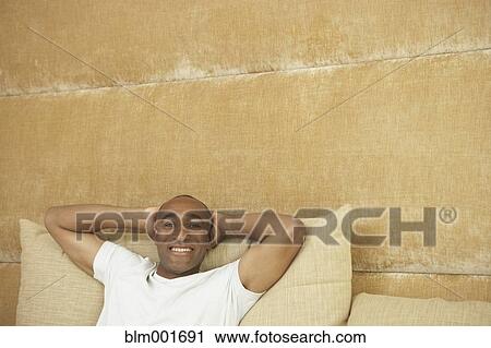 Stock Image - African man with arms behind head in bed. Fotosearch