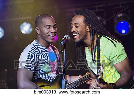 Stock Image - African men singing and playing guitar onstage. Fotosearch