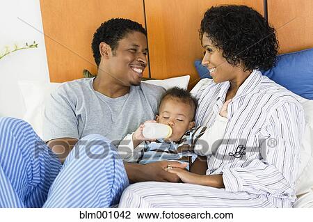 African parents feeding child bottle in bed View Large Photo Image Stock Image - African parents feeding child bottle in bed. Fotosearch