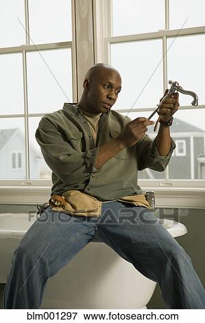 Stock Photo - African plumber repairing faucet. Fotosearch