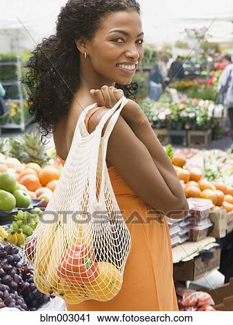 Stock Image - African woman carrying bag of fruits and vegetables. Fotosearch