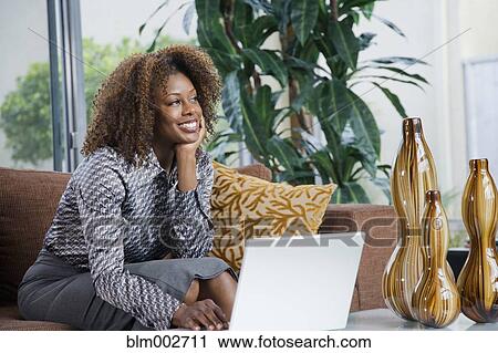Stock Image - African woman daydreaming in modern living room. Fotosearch