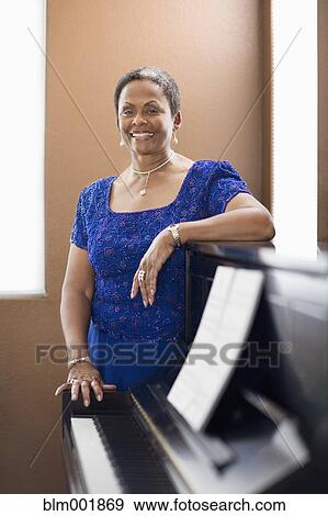 Stock Photo - African woman in evening dress leaning on piano. Fotosearch